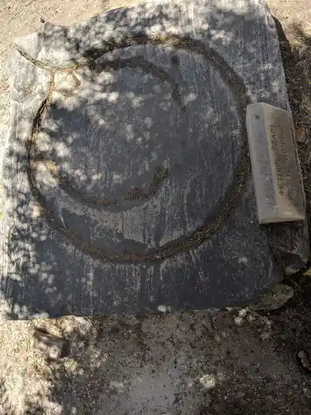 Weathered slab with circular groove and modern Greek inscription in archaeological terrain